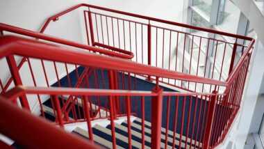 A modern indoor staircase with vibrant red railings and blue carpeted steps.
